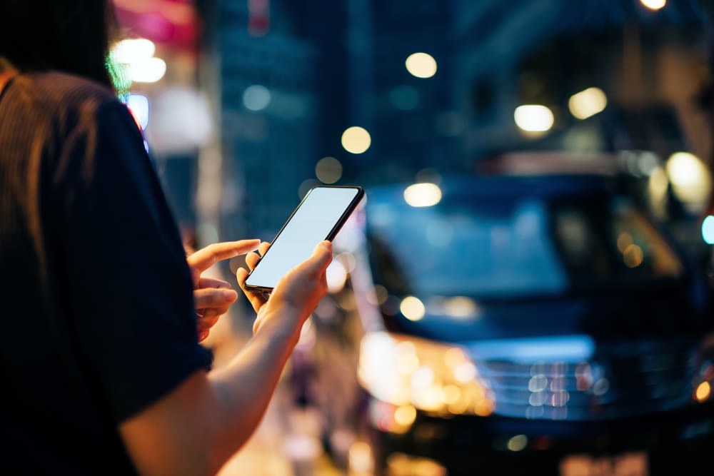 Close up of young woman using mobile app device on smartphone to hail a taxi ride on city street after work in the evening.