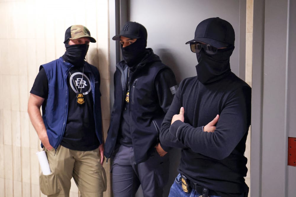 Federal agents wearing face coverings wait outside a courtroom.