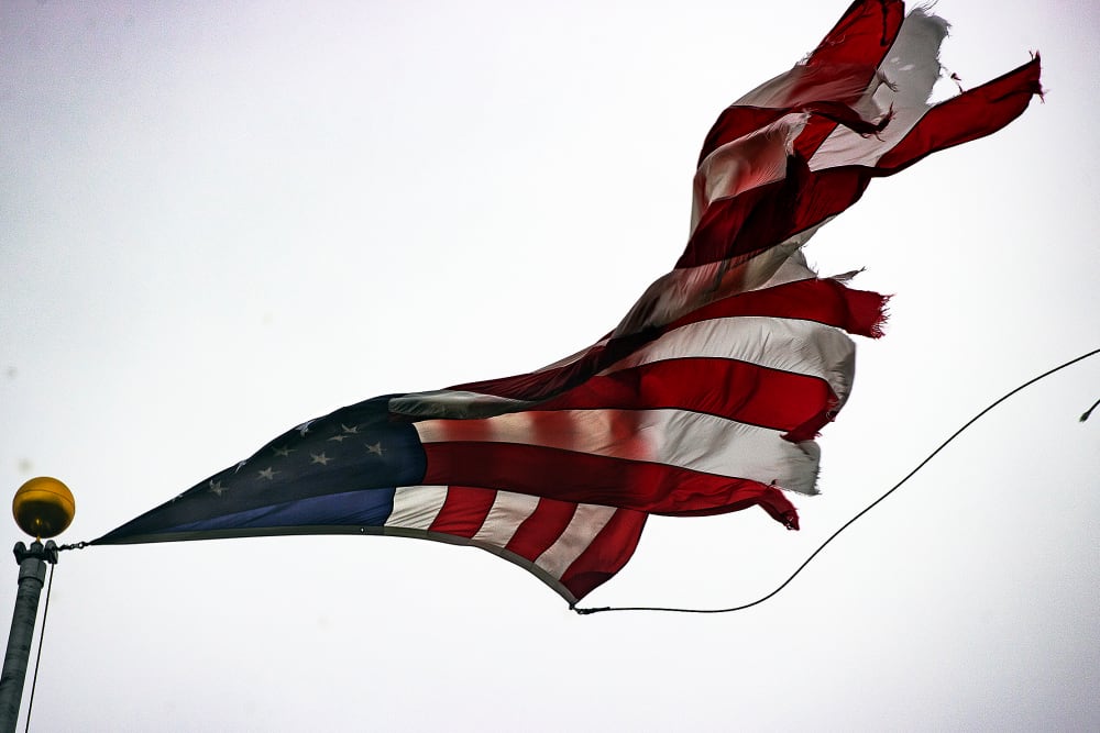 A tattered American flag whips in the wind from a flagpole.