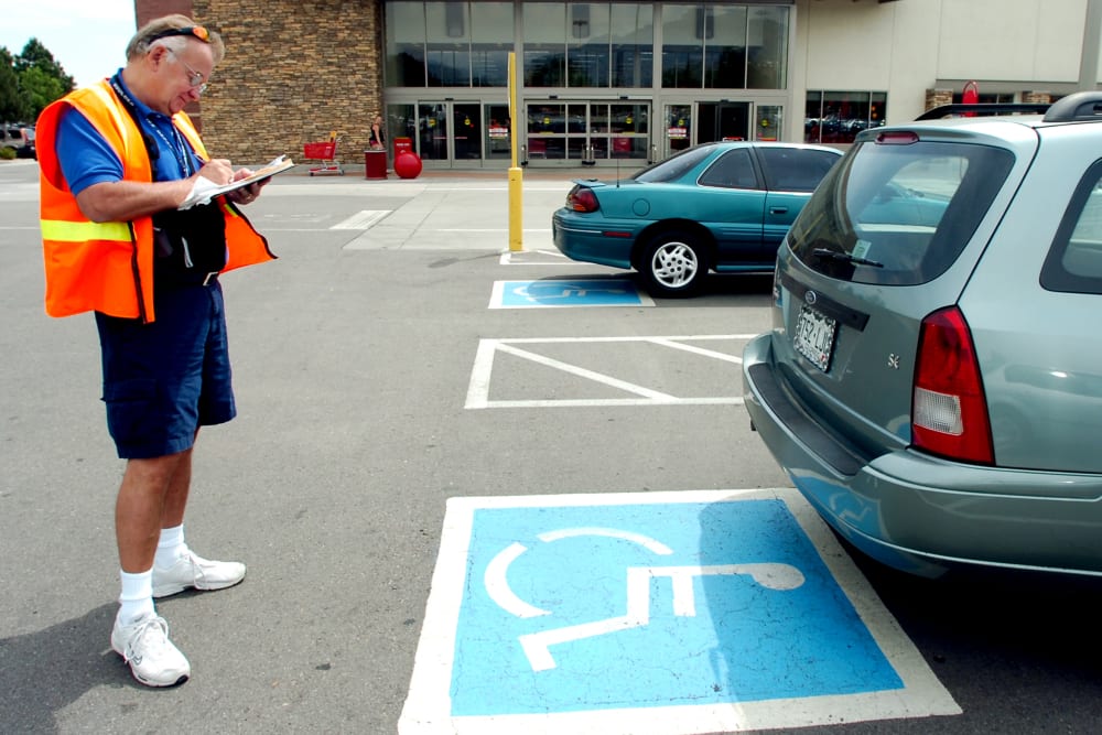 Volunteer handicapped parking enforcement officer writes a parking ticket for a car parked without a handicapped plate or place card.