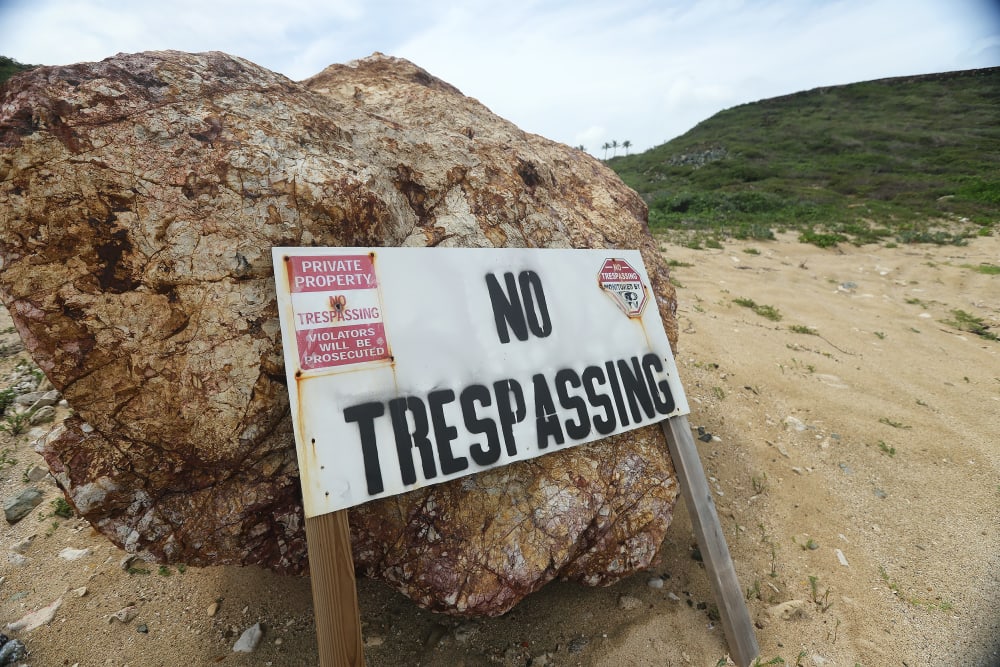 "No Trespassing" sign leaning against a small boulder outside.