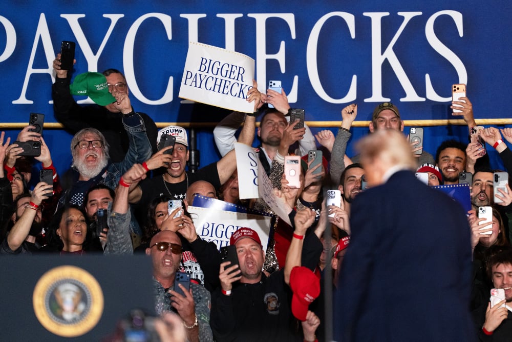 An attendee holds a "Bigger Paychecks" sign during an event on inflation with US President Donald Trump.