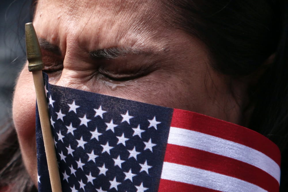 A woman tears up with a small American flag obscuring part of her face.