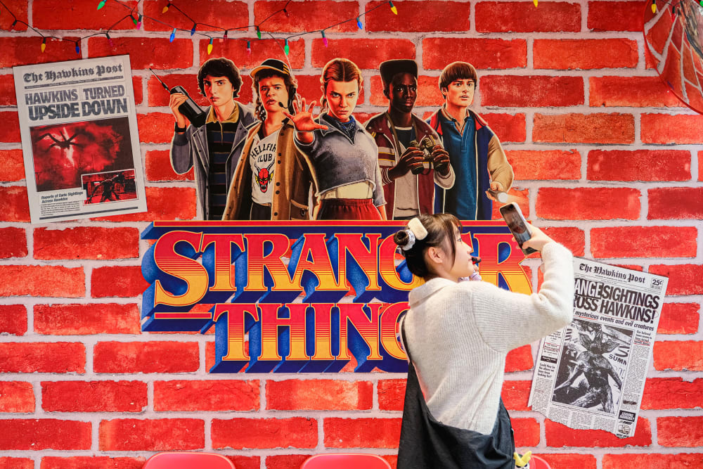 A person takes a photo by a wall embellished with Stranger Things decor.