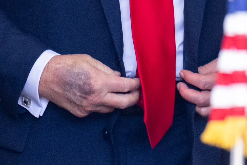 A close-up of Donald Trump’s right hand is seen as he buttons his jacket behind an American flag.