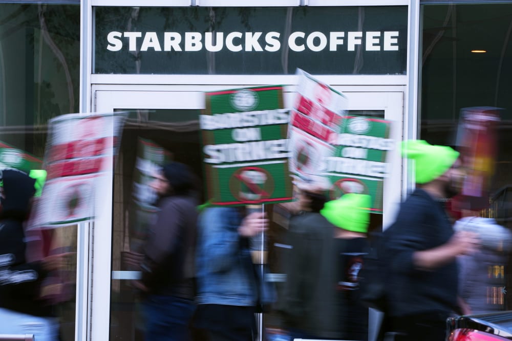 People blurred in motion hold signs in front of a Starbucks Coffee location.