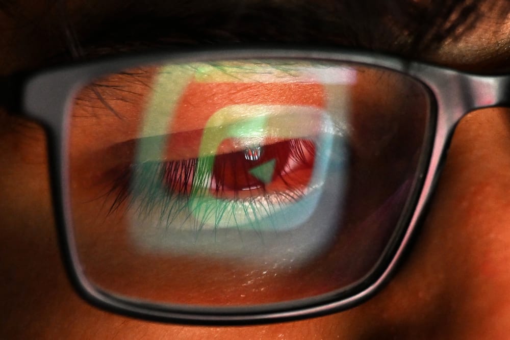 The YouTube logo is reflected in one lens of a person's glasses.