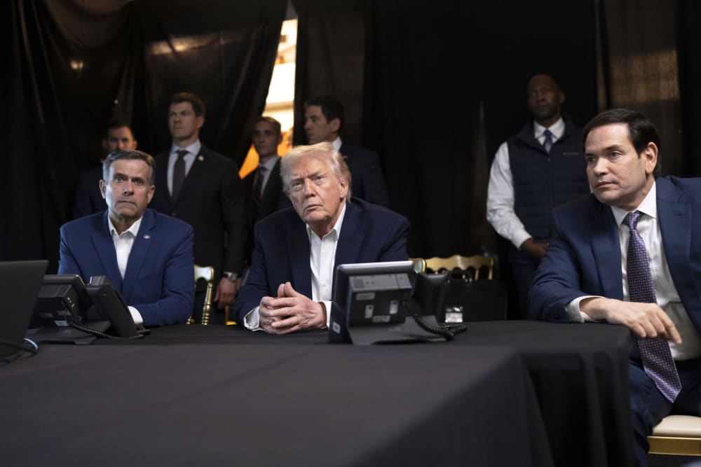 President Donald Trump, center, sits with his hands folded.