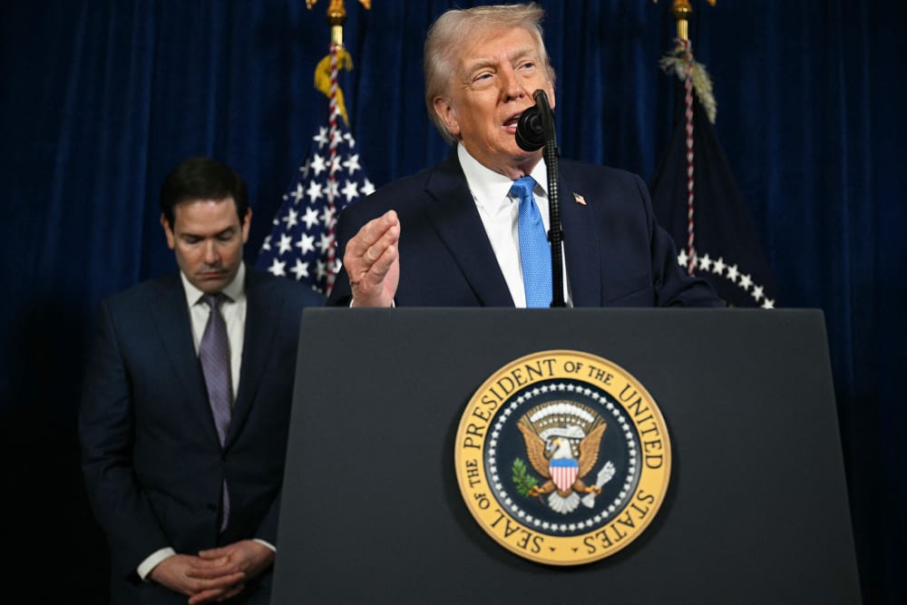 Secretary of State Marco Rubio looks down as President Donald Trump speaks behind a podium.
