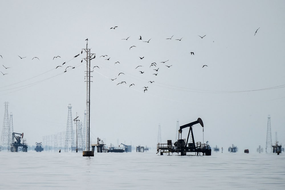 Birds fly over oil platforms in a lake.