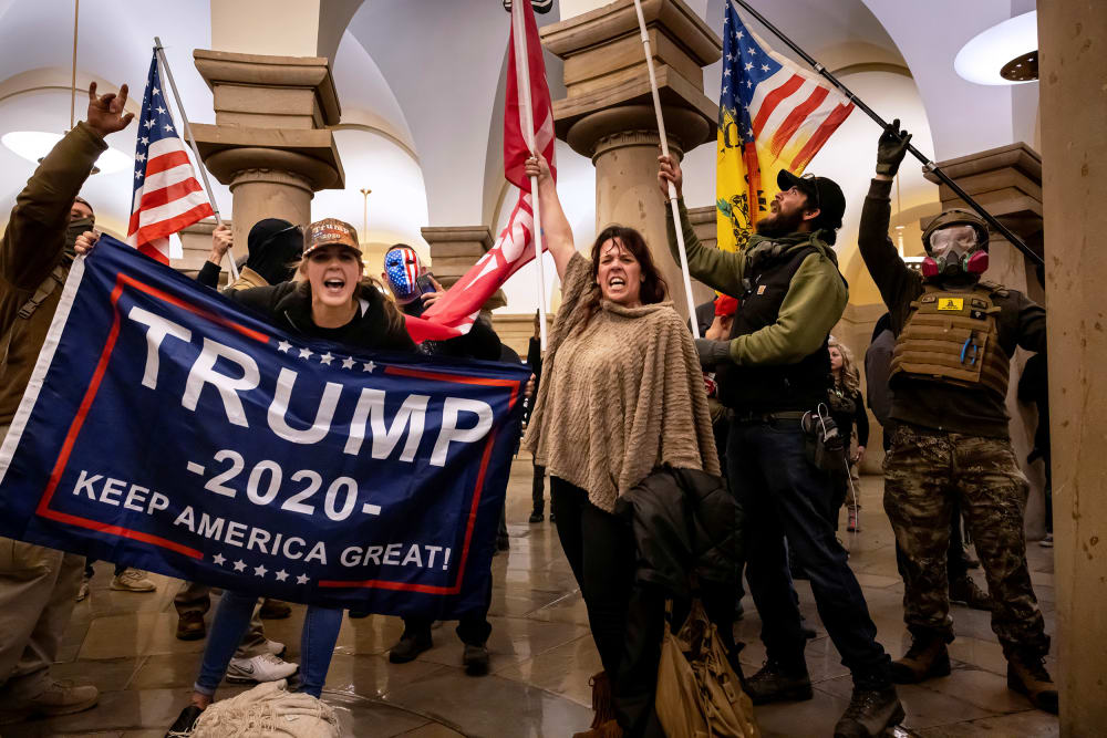 People within the Capitol hold flags supporting Donald Trump.