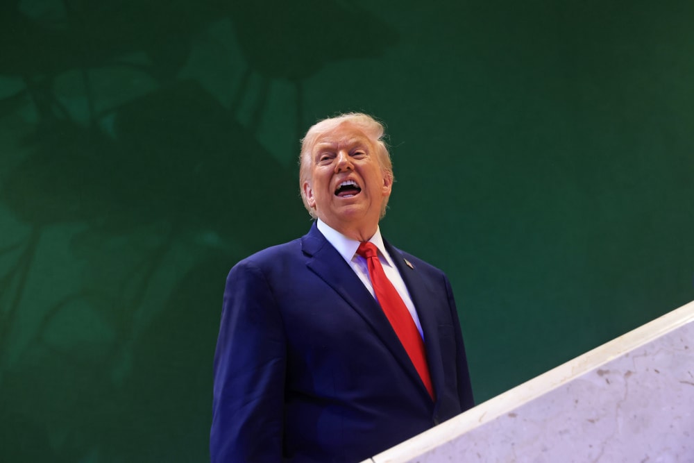 Donald Trump against a green wall, with his mouth open.