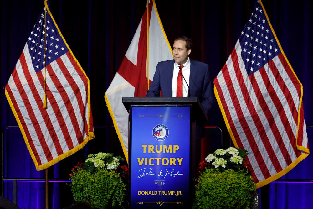 John Wahl stands behind a podium that says "Trump Victory Dinner & Reception with Donald Trump, Jr."