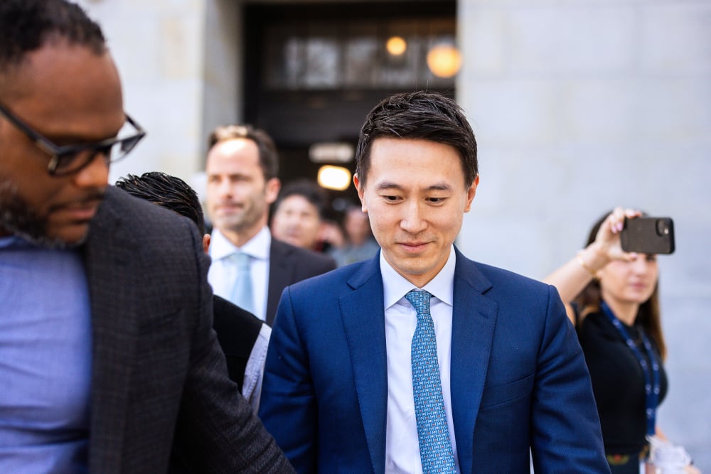 Shou Zi Chew smiling and looking down, surrounded by people.