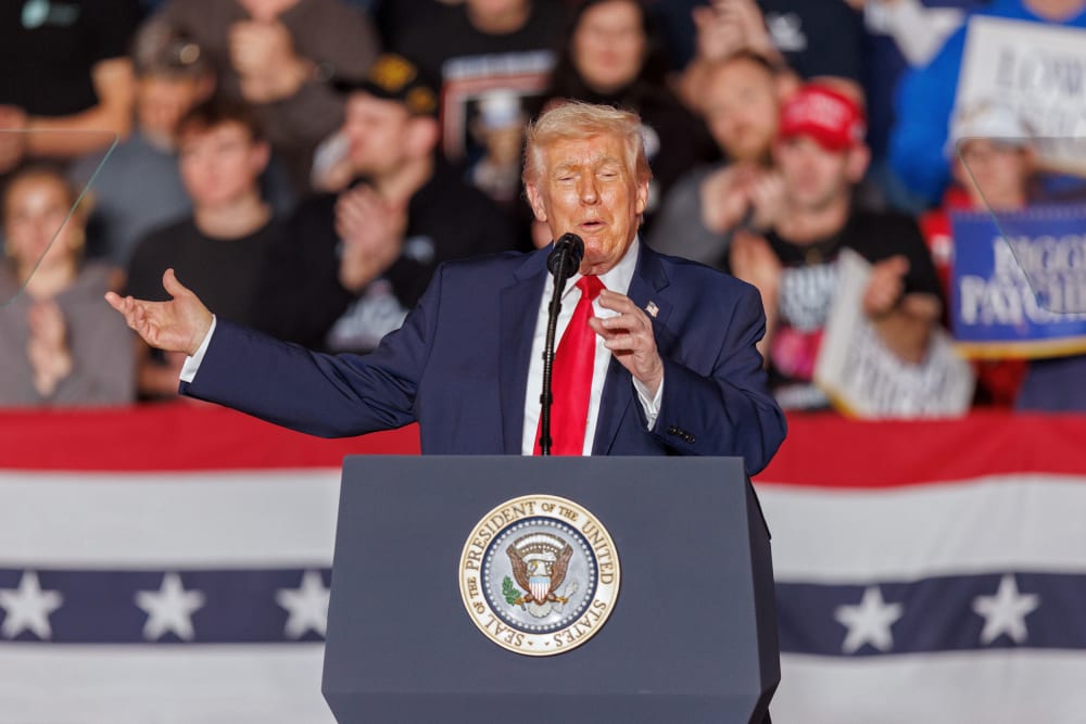 Donald Trump gestures behind a podium in front of an audience.