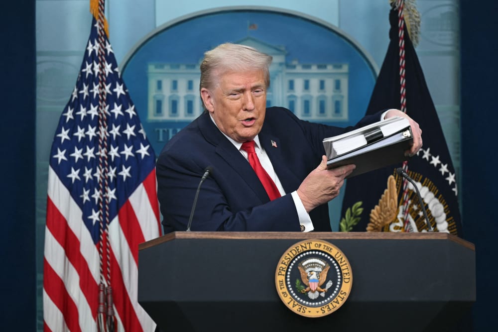 President Trump holds up a folder of documents as he speaks to the media during a briefing.