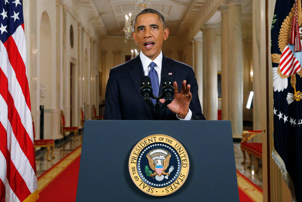 Barack Obama gestures behind a podium and microphone.