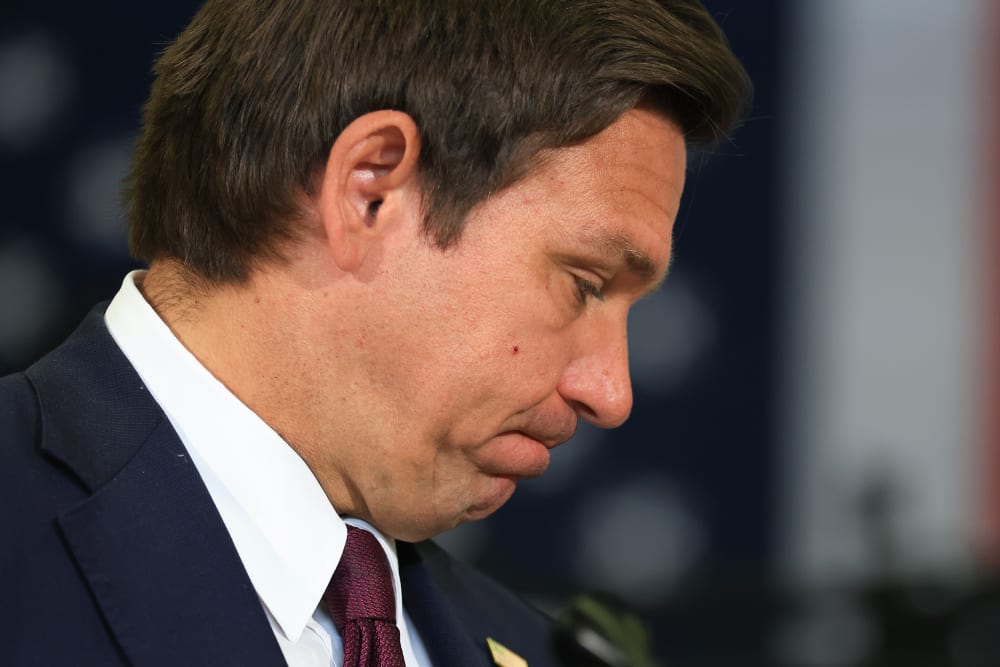 Ron DeSantis, seen in profile, bites his lips with his head down.