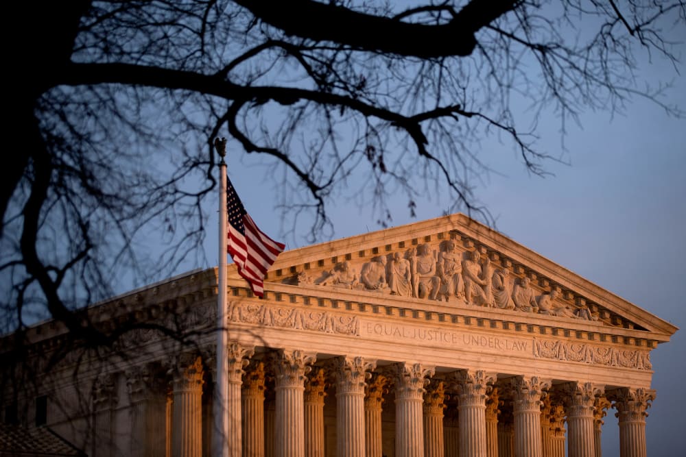 The U.S. flag flies in front of the Supreme Court building at sunset.
