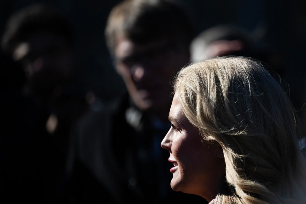 Press secretary Leavitt talks outside the White House, in a frame showing a very tight profile with members of the press in the background.