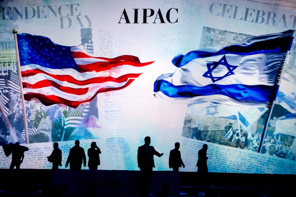 People are silhouetted before a screen that reads "AIPAC" and shows a visual of the American flag and the Israeli flag.
