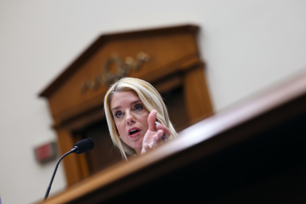 Pam Bondi behind a microphone, partially obscured by the desk in front of her.
