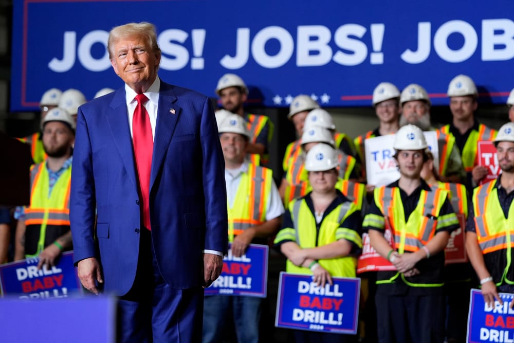 Donald Trump smirks in front of people in hard hats and yellow vests holding signs that say "DRILL BABY DRILL!" Behind them, a large poster that reads "JOBS! JOBS! JOBS!"