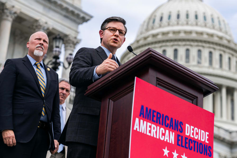 Mike Johnson, right, and Rep. Chip Roy at a podium in front of the Capitol. The podium has a red sign that says "Americans decide American elections."