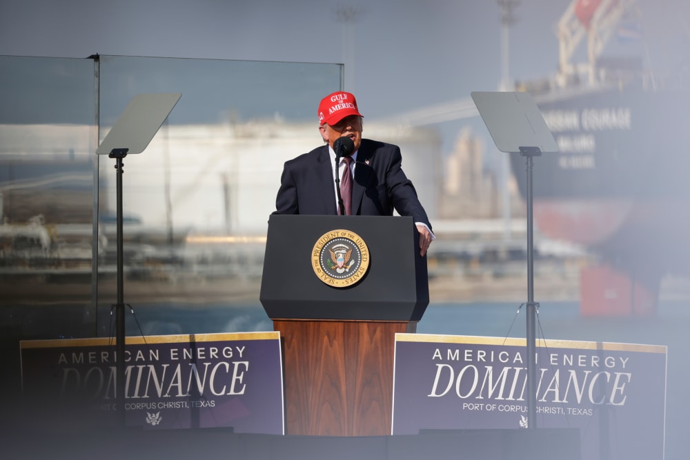 Donald Trump speaks into a microphone at a podium. He's wearing a red hat that says "Gulf of America."