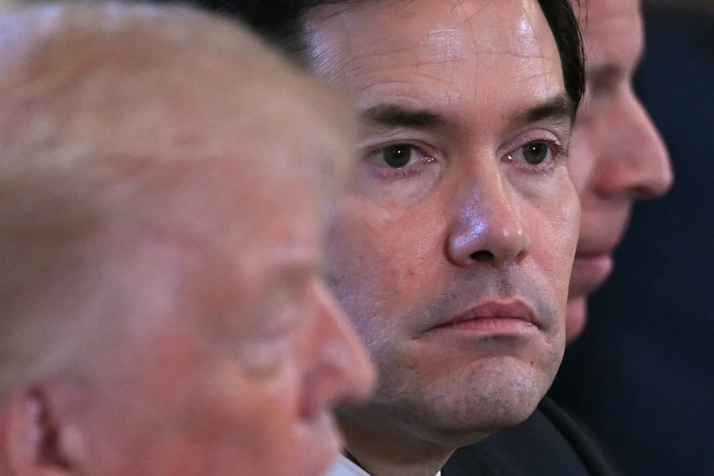 A closeup of Marco Rubio’s face during a meeting in the White House. To his left, Donald Trump can be seen out of focus.