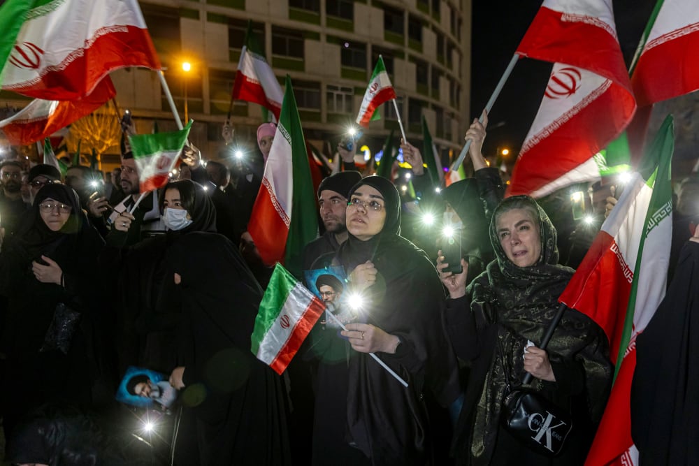 A crowd of people hold pictures of Ayatollah Ali Khamenei and wave Iranian flags.