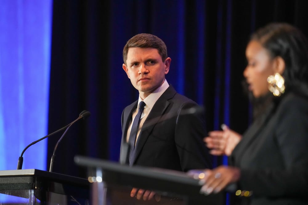James Talarico, in focus, left, looks at Jasmine Crockett, out of focus, right, as she speaks. Both stand at podiums with microphones.