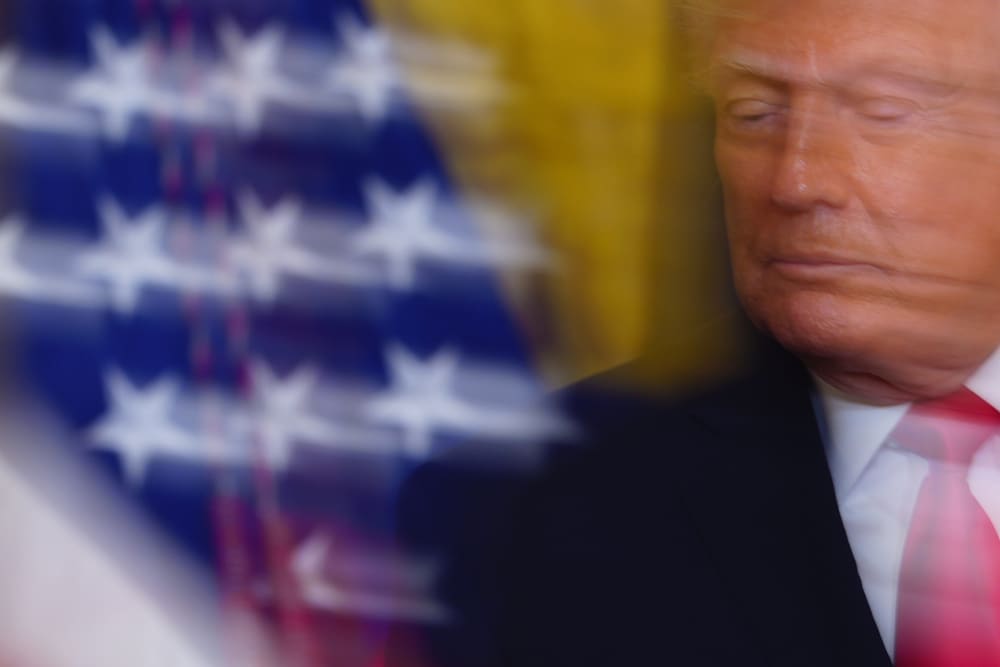 A photo of Donald Trump taken with a slow shutter speed. Part of an American flag is visible on the left-hand side of the photo.