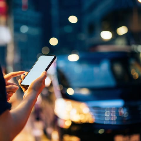 Close up of young woman using mobile app device on smartphone to hail a taxi ride on city street after work in the evening.