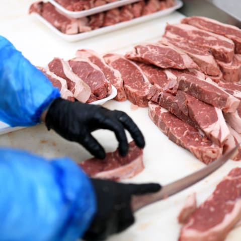 Beef is being trimmed and prepared in a grocery store.