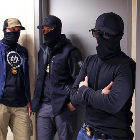Federal agents wearing face coverings wait outside a courtroom.