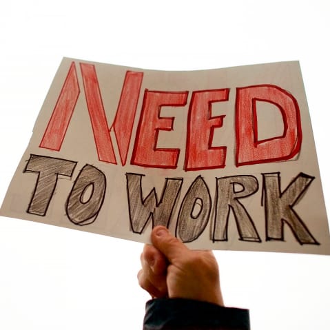 Man holds a sign stating "NEED TO WORK."