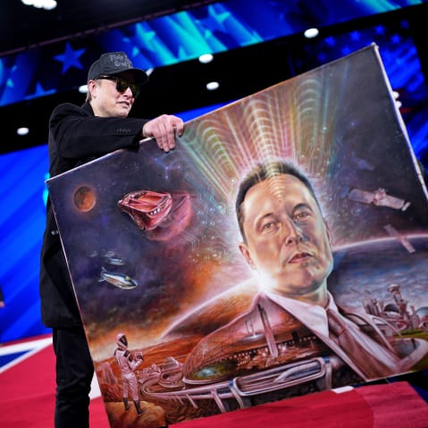 Elon Musk holds a painting of himself.