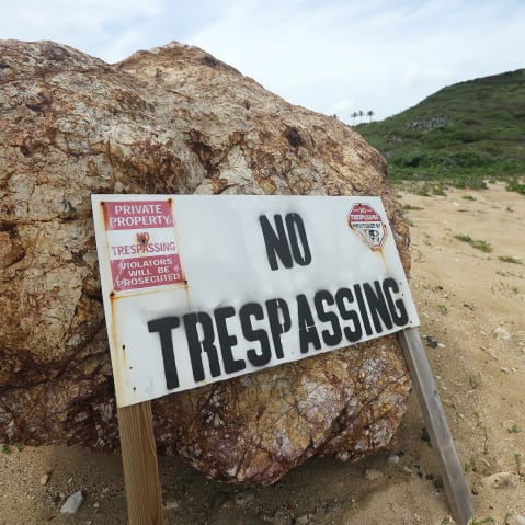 "No Trespassing" sign leaning against a small boulder.