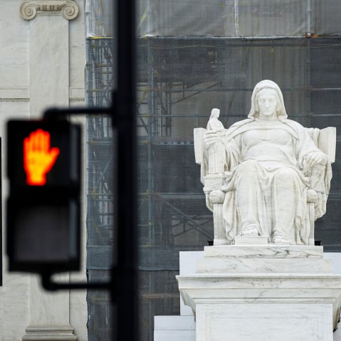 The Contemplation of Justice statue outside the US Supreme Court beside a "Don't Walk" upraised hand symbol in Washington, D.C.