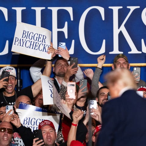 An attendee holds a "Bigger Paychecks" sign during an event on inflation with US President Donald Trump.