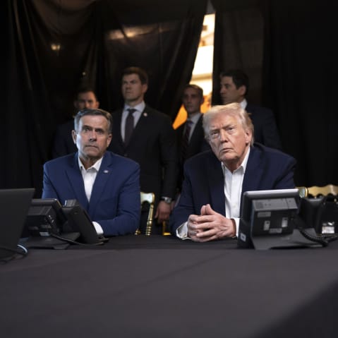 President Donald Trump, center, sits with his hands folded.
