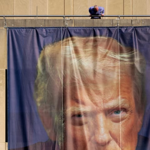 A person inspects a giant banner with the image of President Donald Trump hanging on the outside of the U.S. Department of Labor.