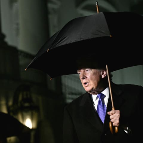 President Trumps walks out of the White House at night, holding a large black umbrella.