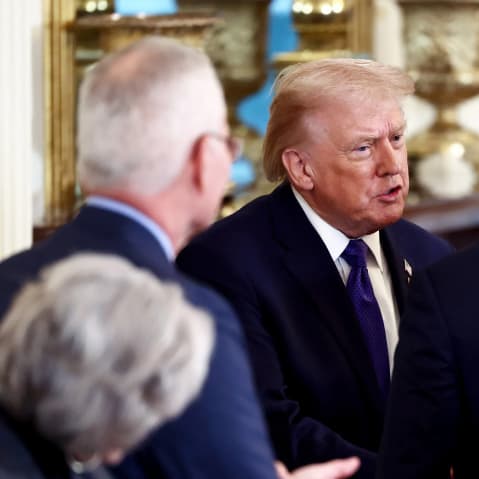 President Donald Trump speaks with people who have their back turned toward the camera.