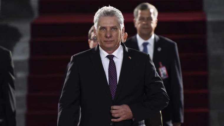 Miguel Díaz-Canel walks toward the camera with his hand on his suit jacket's button.