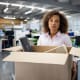 Business woman being fired from her office and carrying a box with her belongings