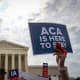 A sign is held up that reads "ACA Is Here To Stay" front of the U.S. Supreme Court.
