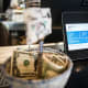 A Square payment device displays tipping options at a coffee shop next to a basket of dollar tips