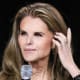 Maria Shriver holds a microphone while seated on stage